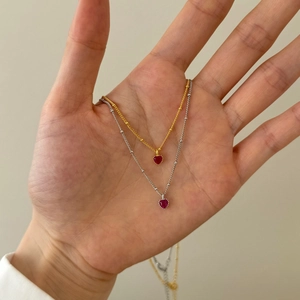 Detail of silver and gold heart necklaces with red gemstones held in hand