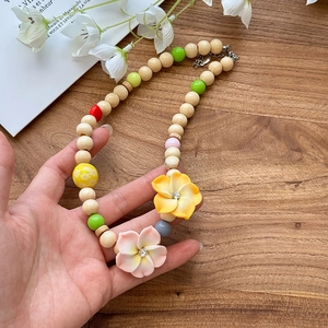 Close-up of vacation-style wooden bead necklace with pink and yellow floral charms.