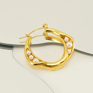 Irregular wavy golden hoop earrings with pearls on a reflective mirror surface