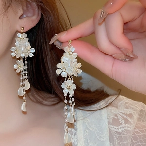 Primer plano de pendientes de borla con flores de tela blanca y detalles de perlas.