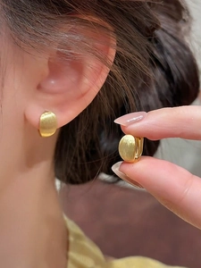 Close-up of golden brushed metal hoop earrings showing texture and secure clasp detail
