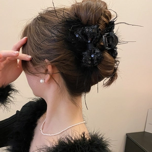 Detail of a black feather bow hair claw clip worn in a sophisticated bun hairstyle