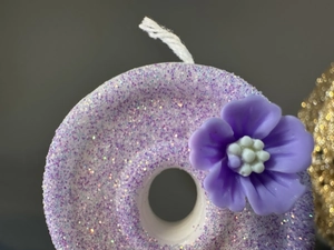 Macro shot of purple donut birthday candle with flower decor and purple glitter finish
