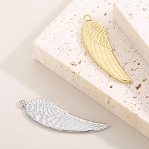 Golden and silver stainless steel angel wing pendants on stone with feather textures