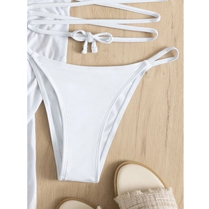 Detail of white bikini set with fringe tassels and sun protection skirt on wooden floor