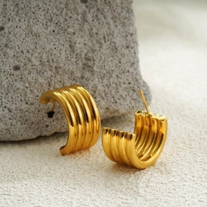 Detailed view of 18K gold hoop earrings with wave texture on a natural stone base