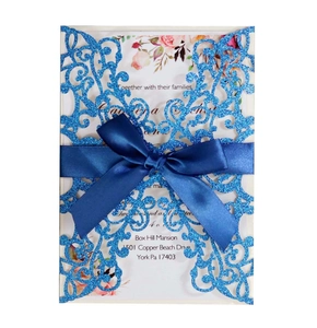 Close-up of laser-cut glitter blue wedding invitation with elegant satin ribbon bow