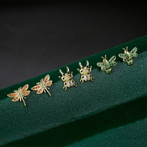 Detailed view of dragonfly, beetle, and bee earrings with zircons on green velvet