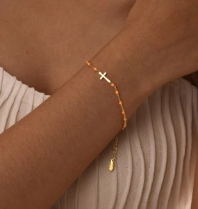 Detail of gold chain bracelet with orange beads and cross charm on a woman's wrist