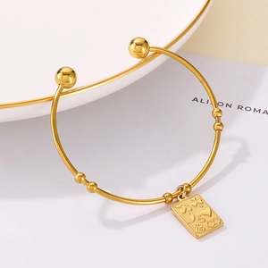 Detail of golden stainless steel open bead bracelet with embossed charms on ceramic