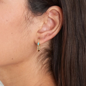 Detail view of a gold oval earring with a rectangular turquoise stone on a female model