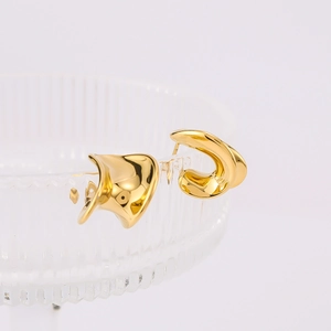 Macro detail of 18K gold plated twisted earrings displayed on clear glass surface