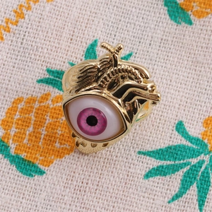 Golden anatomical heart brooch with a purple eye set on a pineapple patterned canvas backdrop