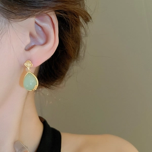 Detailed close-up of light green resin teardrop earrings with golden cloud motif on model