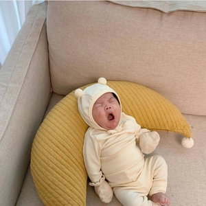 Cozy moon-shaped cotton nursing pillow and yellow newborn romper on a soft beige sofa