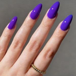 Macro view of glossy deep purple almond-shaped press-on nails with a gold twisted ring