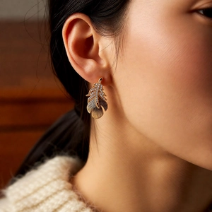 Detailed shot of an 18k gold plated feather earring with inlaid sparkling crystals on a model