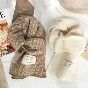 Détail d'écharpes en maille à chevrons camel et blanc cassé avec étiquettes tissées