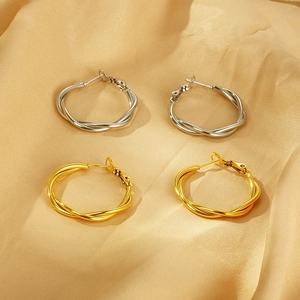 Detailed close-up of gold and silver twisted rope hoop earrings on soft yellow silk fabric