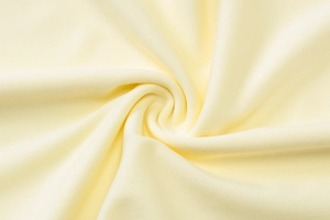Detailed macro view of pale yellow knitted fabric texture with a soft spiral draping effect