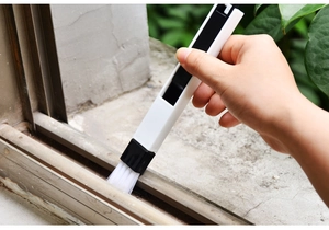 Detailed view of handheld window groove brush cleaning dust from white metal tracks