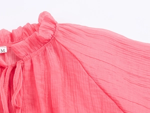 Detail of coral pink ruffled stand collar and tie neck with pleated fabric texture