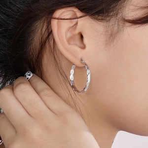 Polished silver stainless steel hoop earrings with twisted design worn by a model