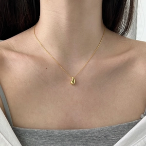 Close-up of a minimalist gold teardrop pendant necklace worn by a fashion model