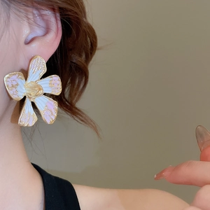 Close-up of a delicate pink and white floral earring with golden frame on a model