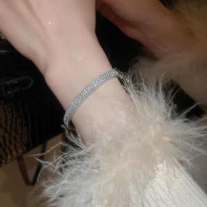 Silver bracelet with rectangular cubic zirconia inlay worn against a feather cuff and leather bag