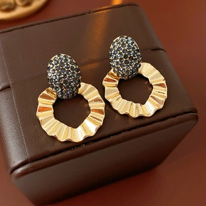 Detailed close-up of gold wavy hoop earrings with blue pavé oval stud on a leather case