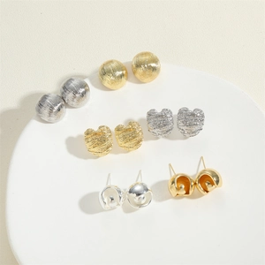 Detailed close-up of textured heart and hollow sphere earrings on a white pedestal