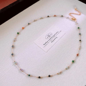 Close-up of golden chain necklace featuring colorful faceted crystal beads on white fabric