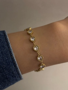 Detail of gold heart bracelet with inlaid zircons worn on wrist with denim cuff