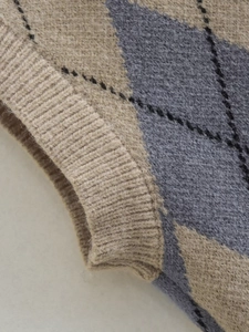 Detail of argyle knit vest featuring khaki and grey diamond patterns and ribbed hem