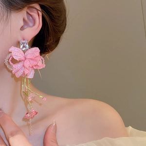 Close-up of pink fabric flower earrings with long tassels and crystal studs on model