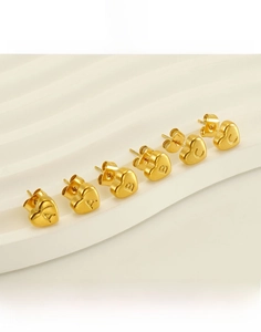 Detail of gold heart earrings with A, B, and C letters on a white textured stand