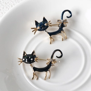 Colorful enamel cat brooches in black and blue with rhinestones on a ceramic dish