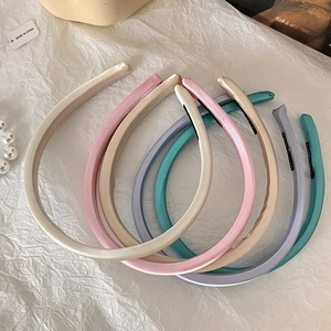 Flat lay of multiple satin padded headbands in various candy colors on white textured paper