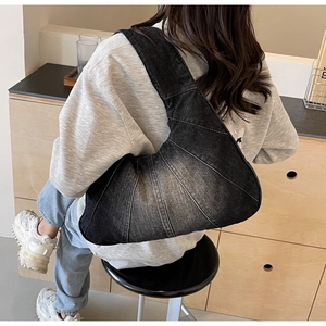 Vue latérale d'un sac croissant en denim noir porté par un mannequin dans un café