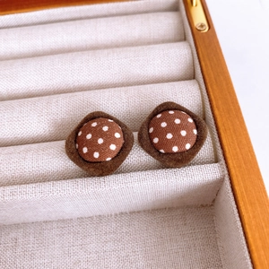 Close-up of brown diamond-shaped fabric stud earrings with polka dots and plush trim