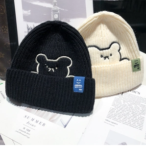 Detail of knit beanies in black and beige with cute bear embroidery and texture