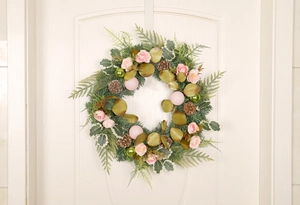 Close-up of artificial Christmas wreath with pink roses and pine cones on a white door