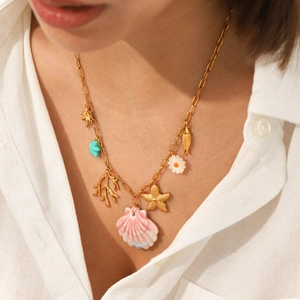 Gold starfish and shell pendant necklace on model wearing a white shirt