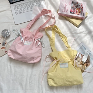 Detail of pink and yellow canvas tote bags with drawstring ribbons on white fabric