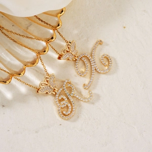 Golden butterfly and zircon initial necklace set on a shell with elegant sand background