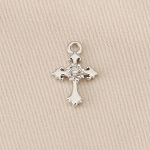 Detailed view of silver cross pendant with center zircon on textured beige fabric