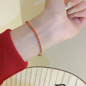 Close-up of a handmade red woven bracelet with gold beads and traditional Chinese fan
