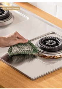 Close-up of flexible green silicone brush cleaning a stainless steel gas stove surface