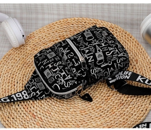 Detail view of black crossbody chest bag with white letter print and multi-zipper pockets